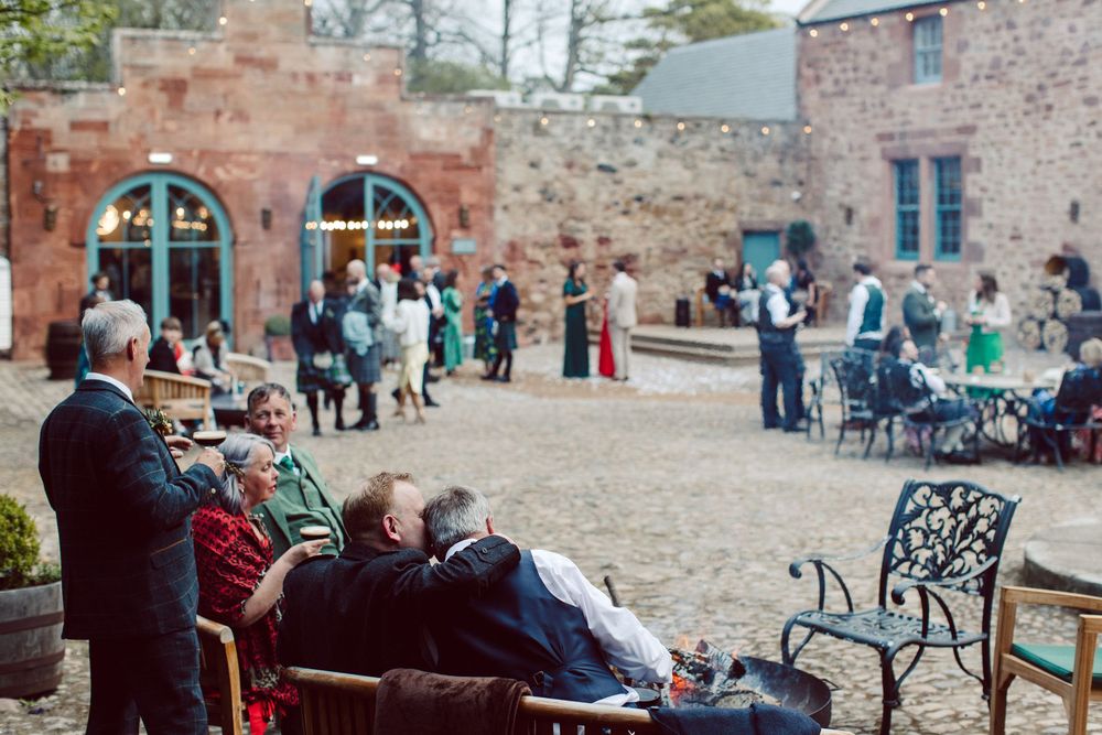 Visitors relax and socialize in the courtyard of a historic brick building with arched windows and outdoor seating.