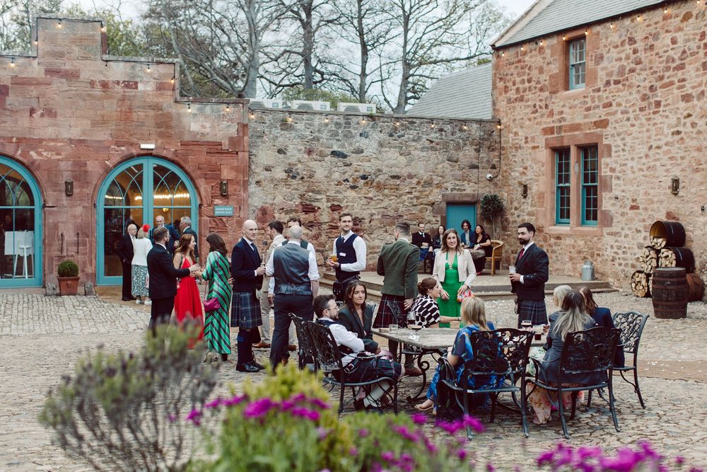 Wedding guests gather in a rustic courtyard with stone walls and arched doorways surrounded by lavender flowers.