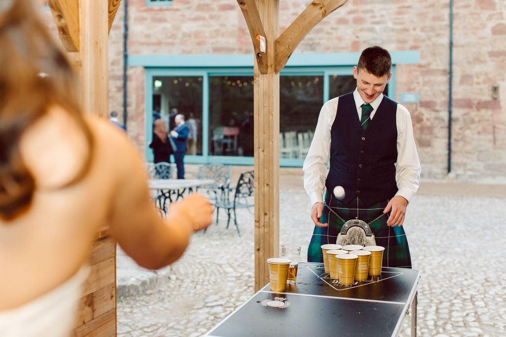 Bartender in formal attire pouring drinks at an outdoor brick venue with teal accents.
