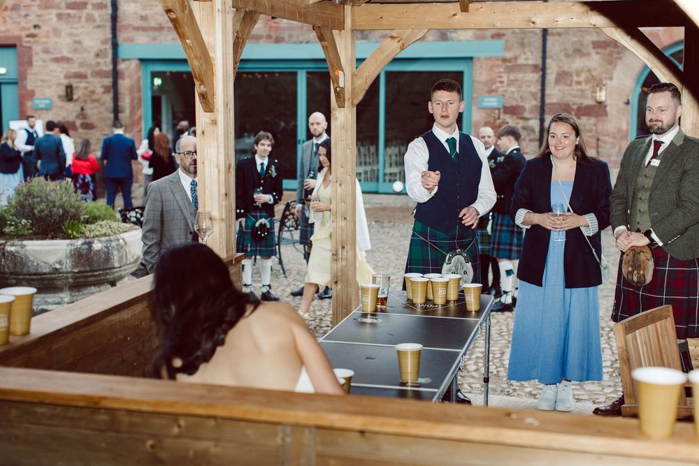 Guests mingling under a rustic wooden pavilion with exposed brick walls at an outdoor event.