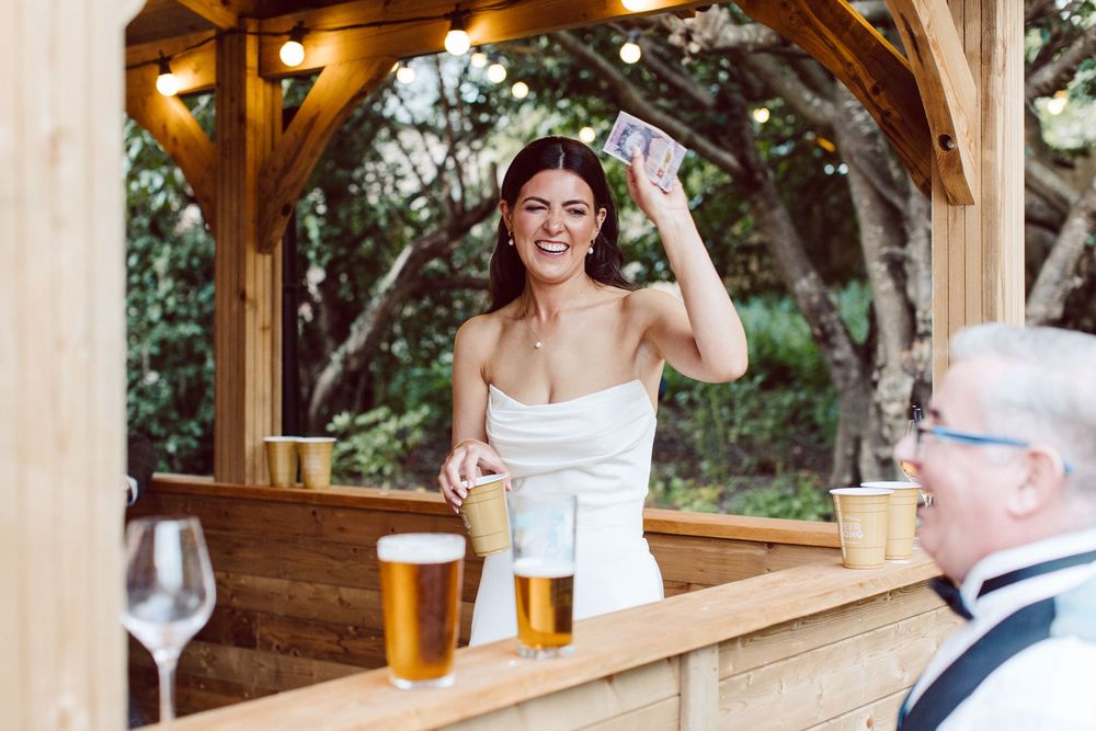 People enjoying drinks and conversation at a rustic wooden outdoor bar patio during a sunny day.