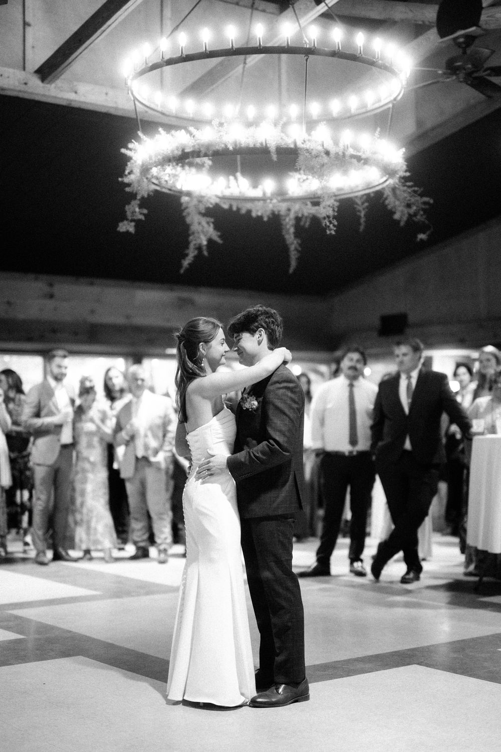 Black and white photos show couples dancing at a wedding reception under elegant circular chandeliers.