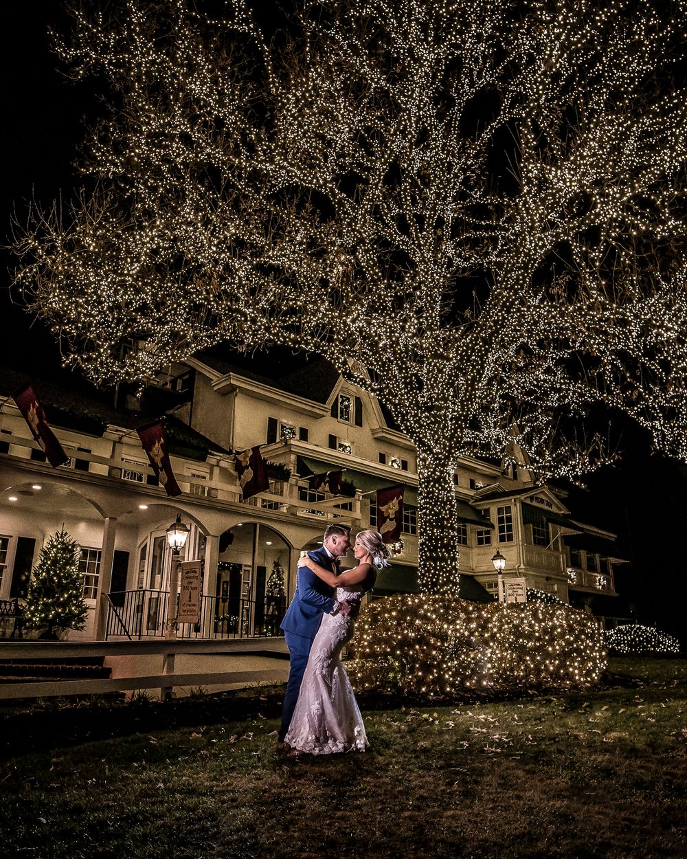 Romantic nighttime scene with twinkling lights illuminating a couple dancing on a lawn near historic houses.