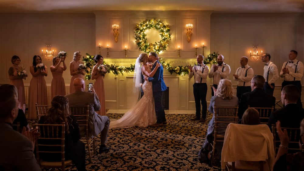 Wedding reception venue decorated with warm lighting and floral arrangements showing dance floor and guest tables.