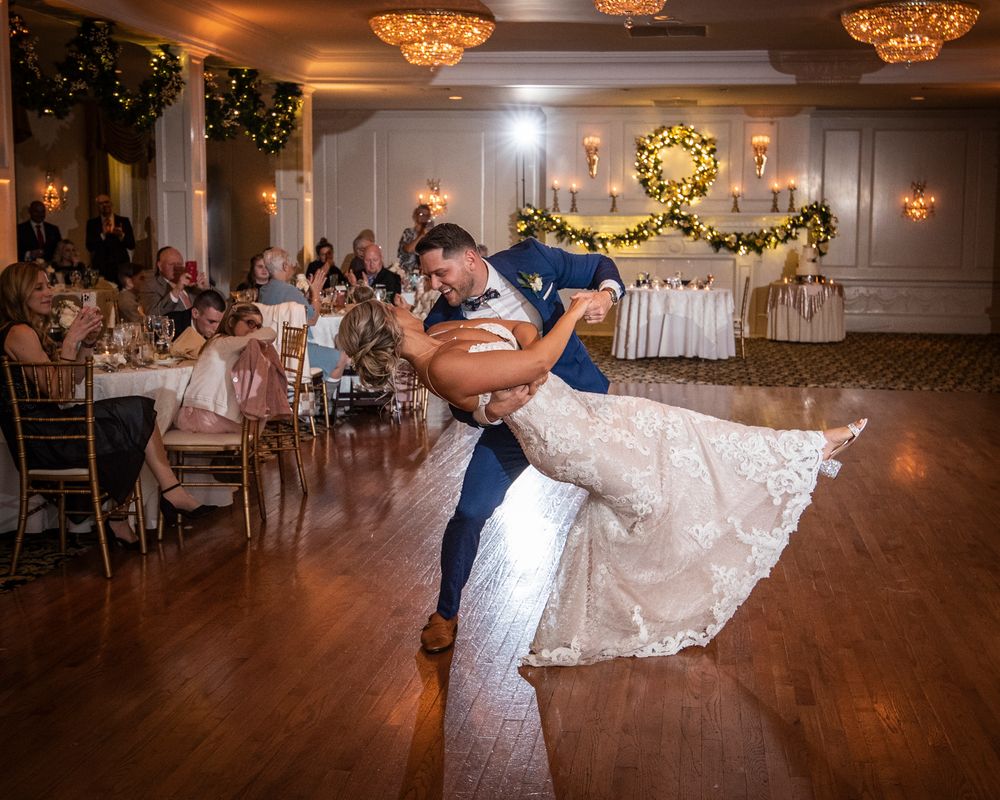 A couple performs a romantic dip during their first dance on a wooden dance floor at an elegant reception venue.