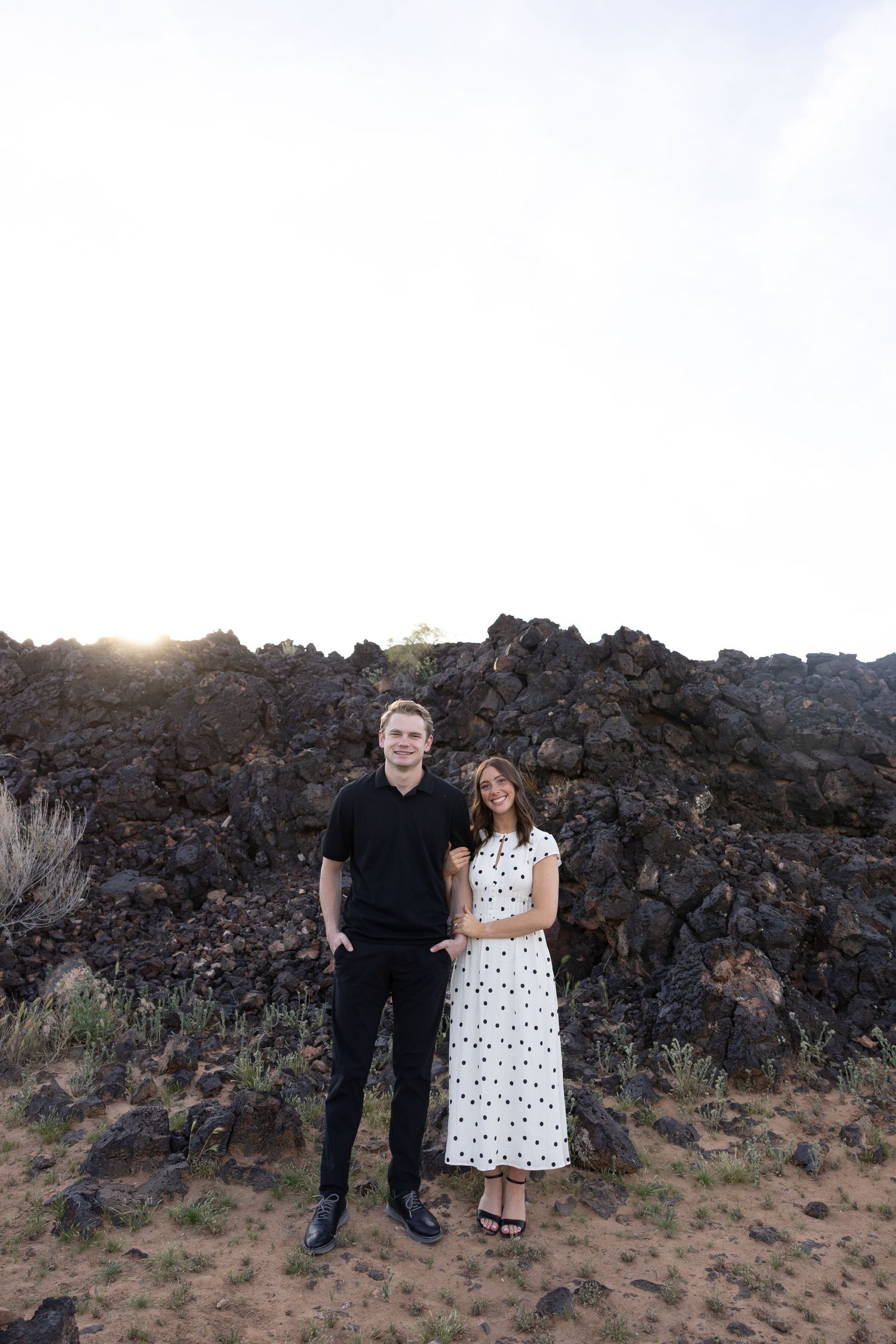 A couple poses together against a rocky volcanic landscape backdrop during sunset.