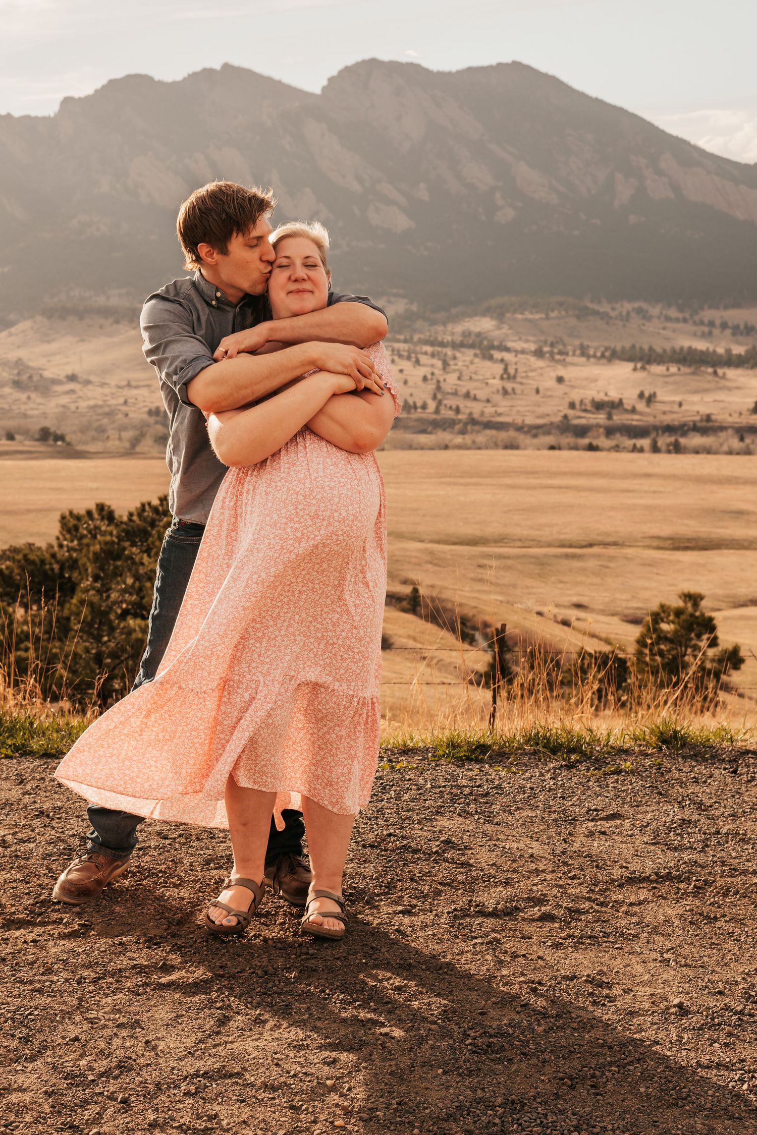Couple embracing in golden fields with Rocky Mountain flatirons | Maternity Photos in Boulder Colorado