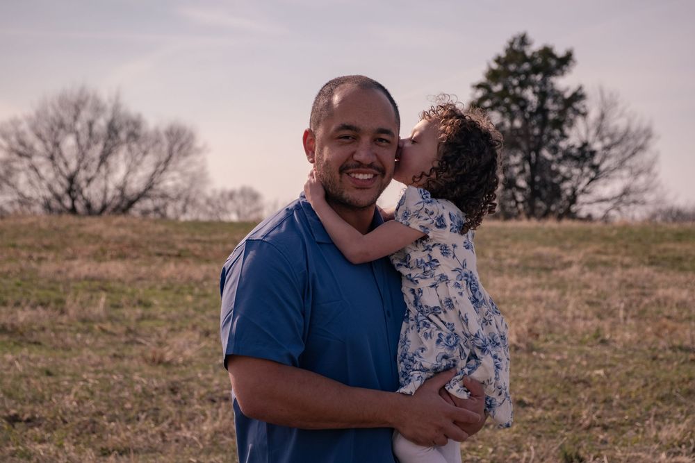 A couple embraces in a sunny outdoor field during a romantic photoshoot at golden hour.