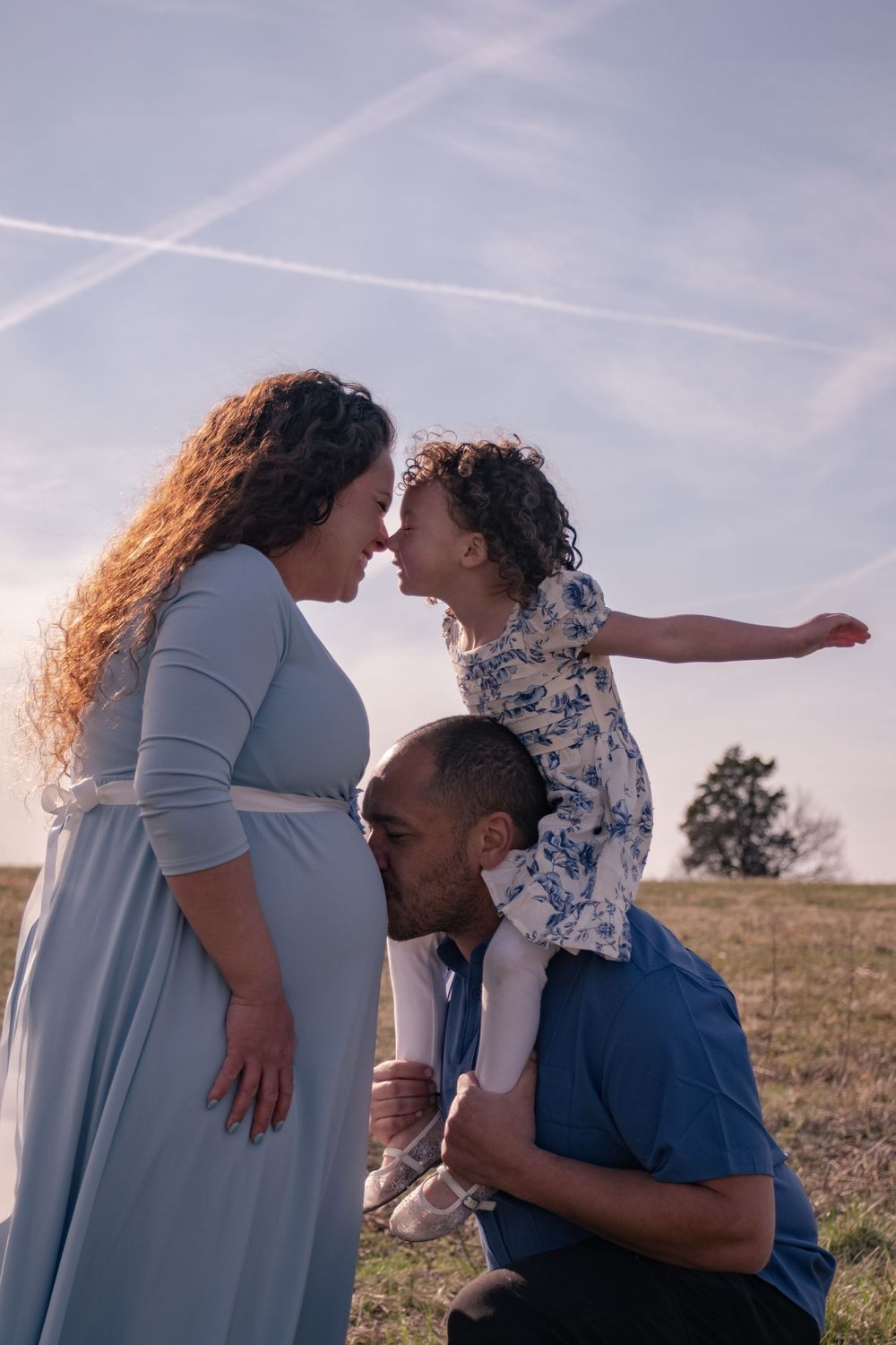 A tender family moment shared outdoors against a sunset sky with airplane trails.