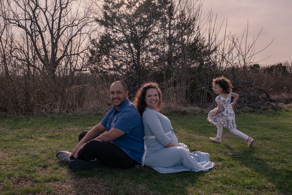 A peaceful sunset scene in a grassy field with people relaxing while a child runs playfully in the background.
