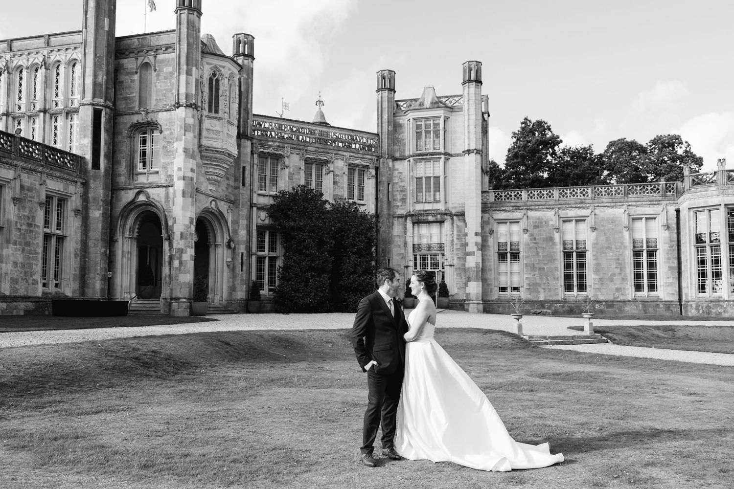 A black and white photograph of a romantic wedding moment in front of a High Cliffe Castle Dorset. Gothic-style stone castle.