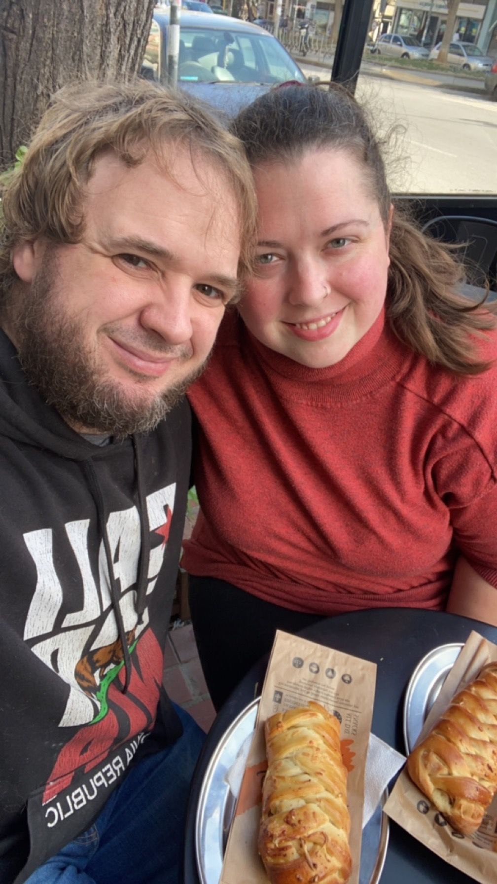 A couple enjoying pastries together while taking selfies in a car.