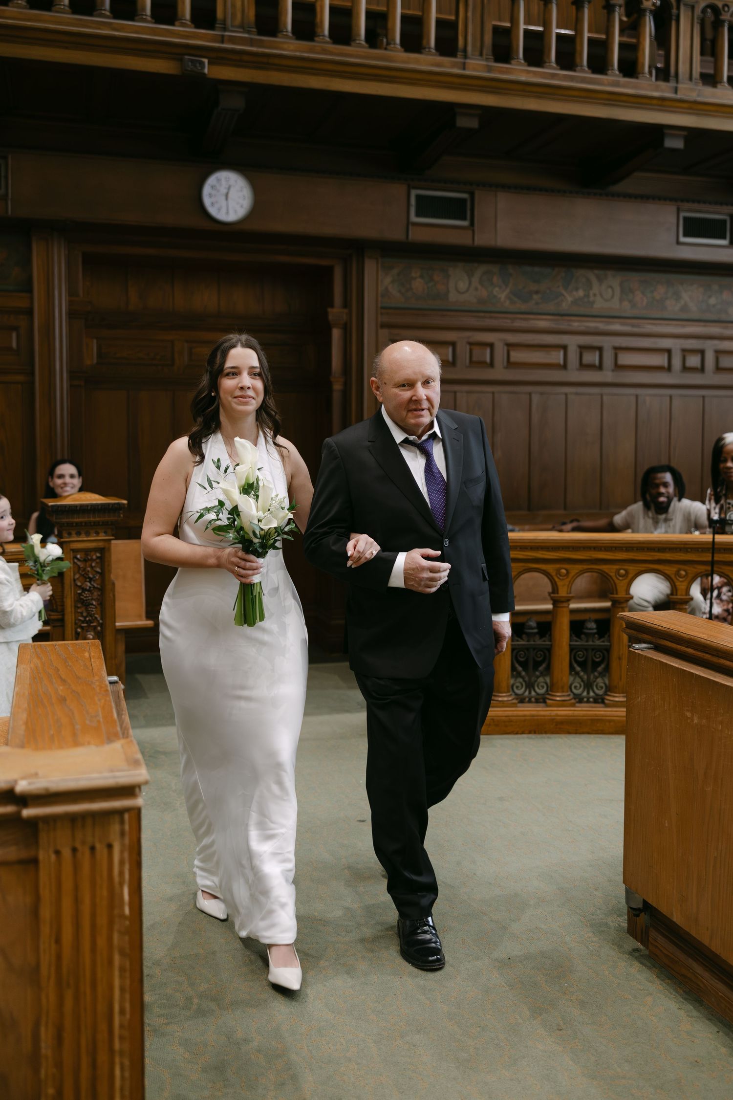 Wedding couple walks through a church interior with wooden pews and carpeted floors.The old city hall Toronto wedding photographer Daria