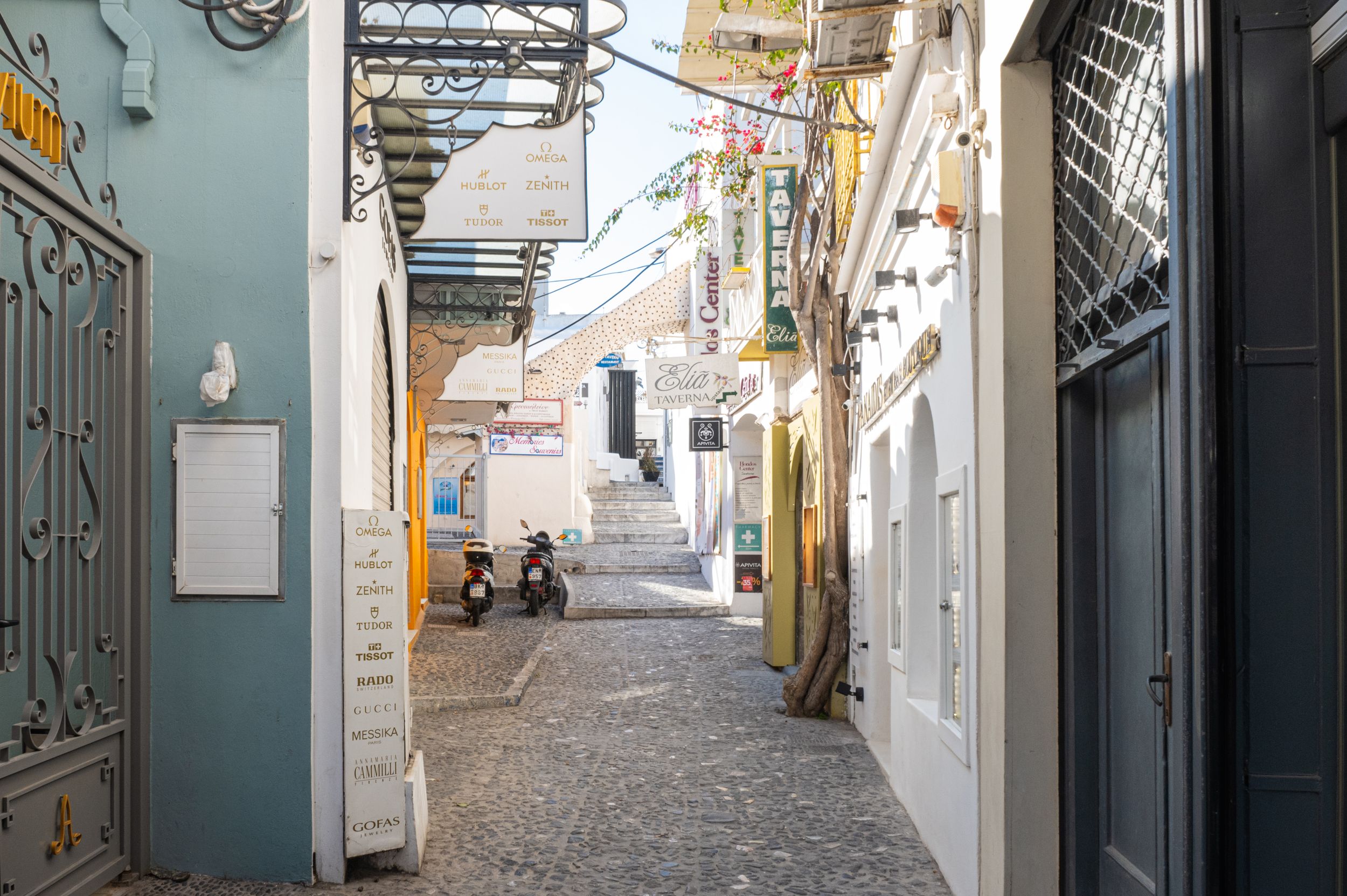 Narrow whitewashed alley with blue doors and stone steps in a Mediterranean village on a sunny day.