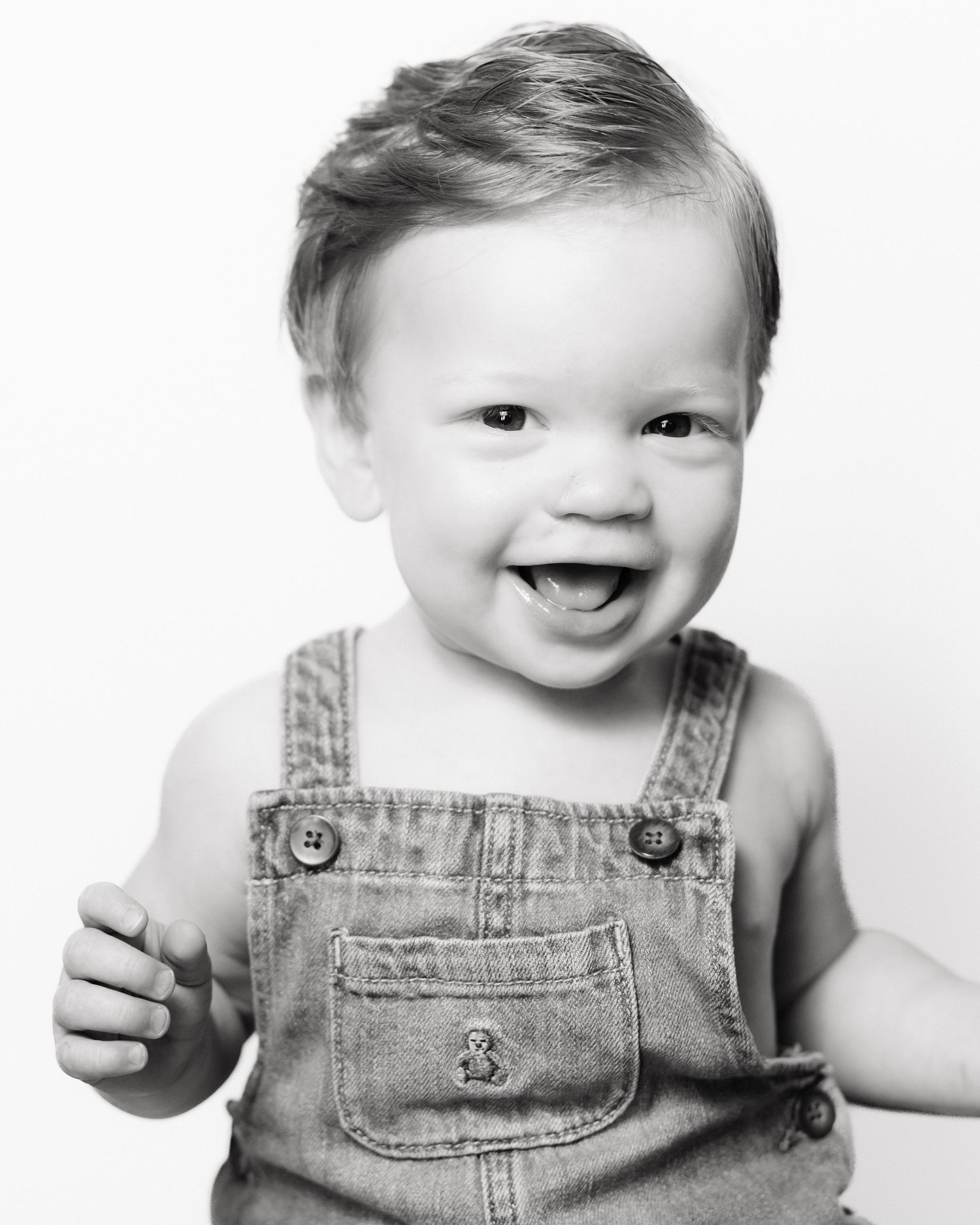 A series of three black and white photos showing a baby wearing denim overalls with joyful expressions.