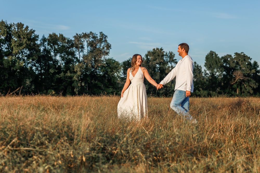 A couple holds hands while walking through a golden field at sunset, creating a romantic silhouette against the sky.
