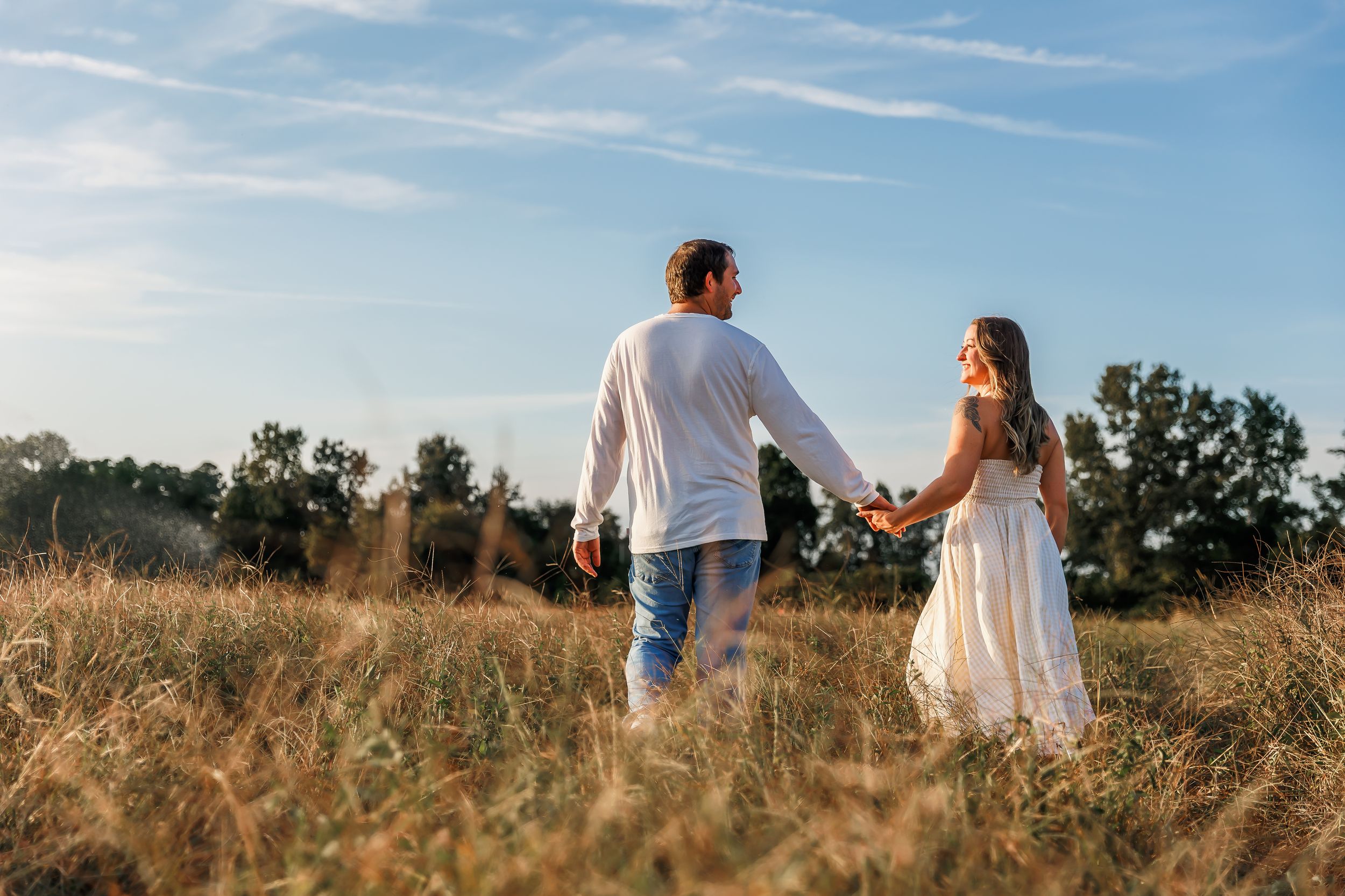 A couple walks together through a golden field at sunset holding hands and enjoying the peaceful countryside scenery.