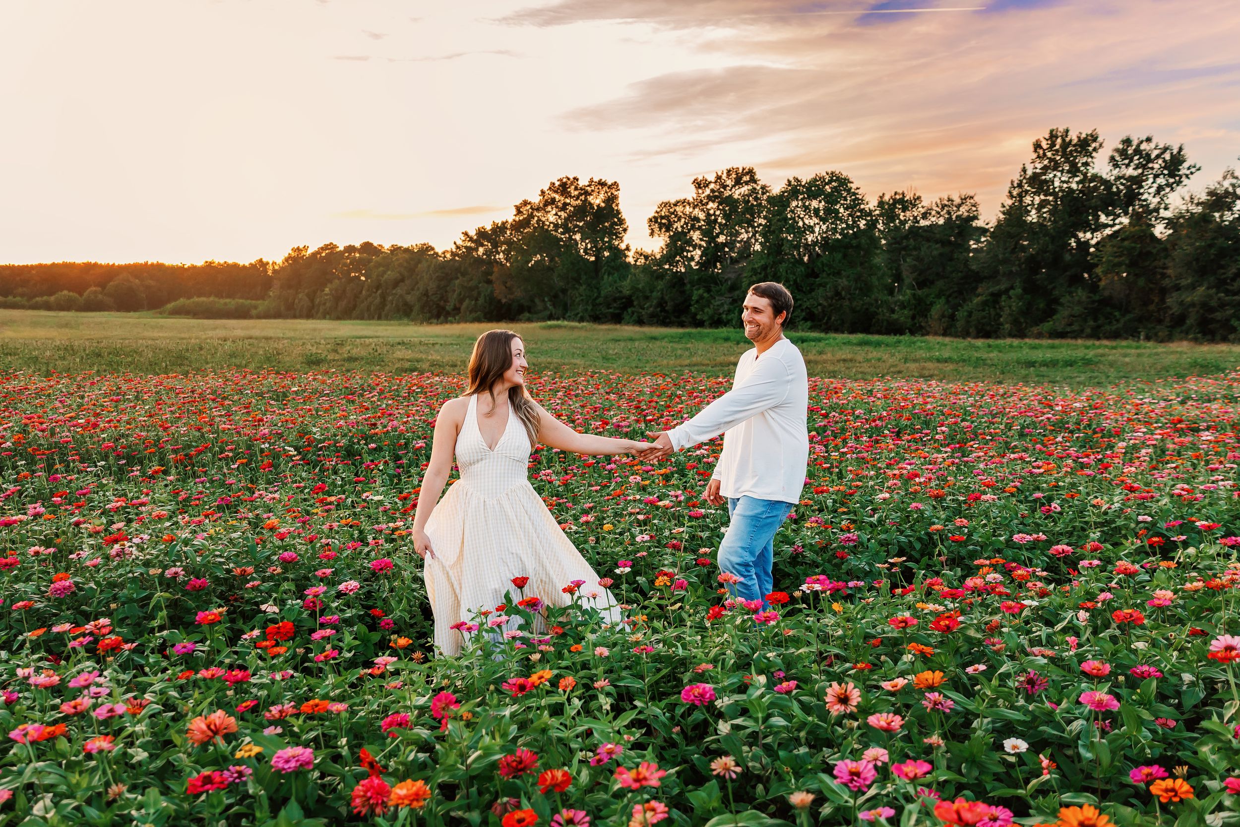 A couple stands together in a vibrant field of red wildflowers at sunset with trees in the background.
