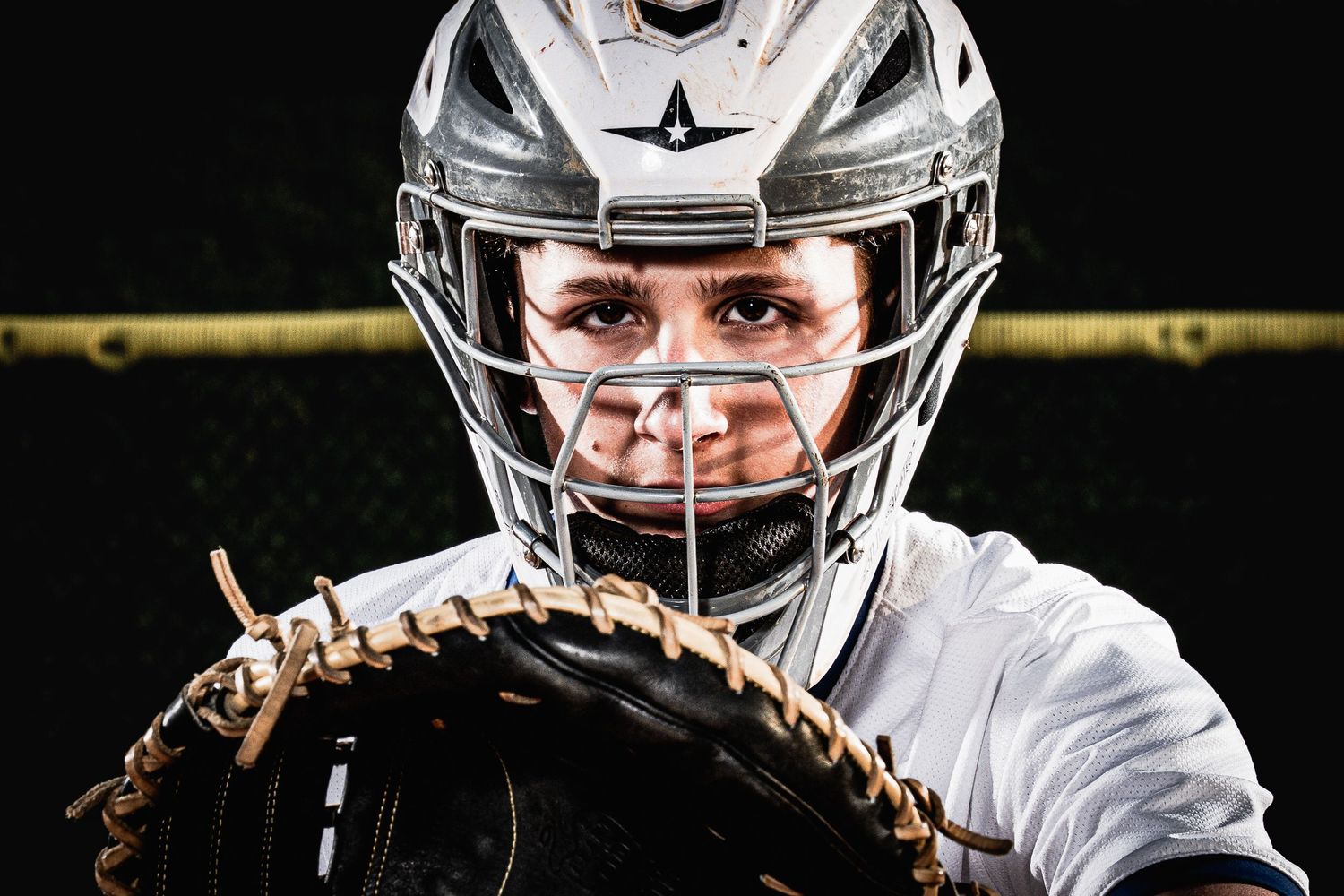 Female softball catcher in helmet and glove ready to catch, intense focus, dark background.
