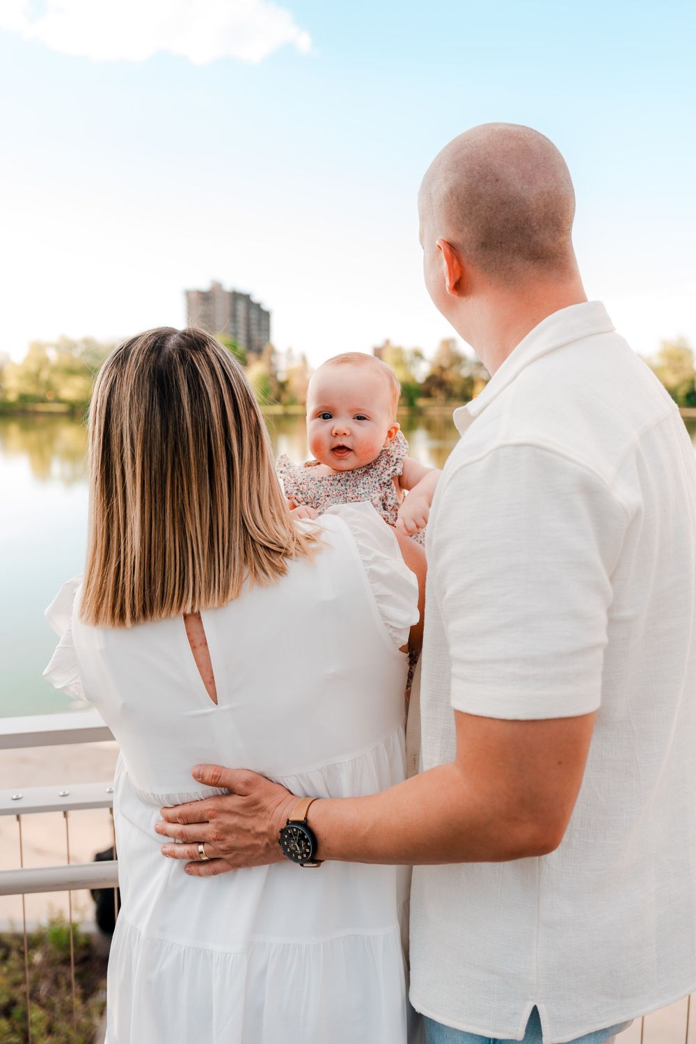 Family with baby enjoying a scenic lakeside view on a sunny day.