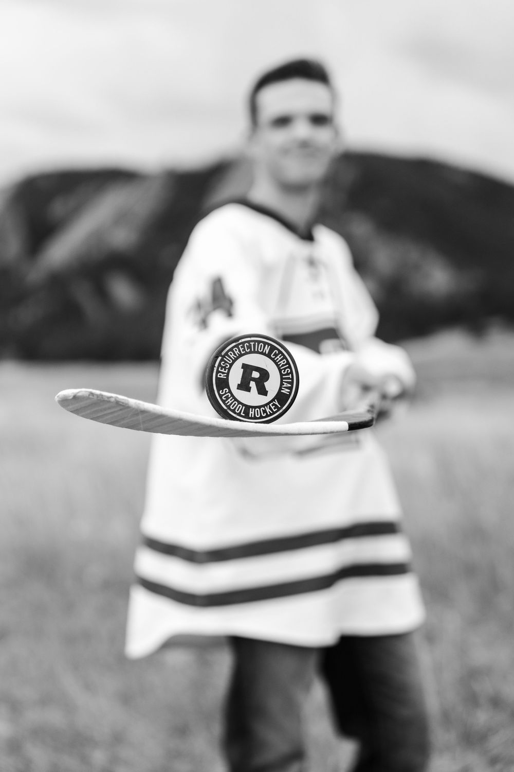 Black and white photo of young man in hockey jersey holding stick with puck in field.