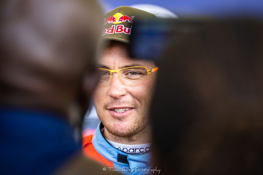 Racing driver wearing a Red Bull cap smiles during a Formula 1 event.