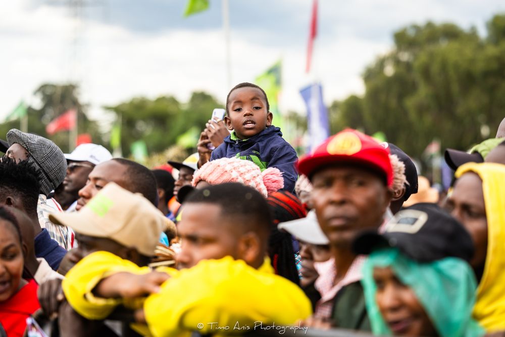 A large crowd of spectators watches an outdoor sporting event while wearing colorful clothing and hats.