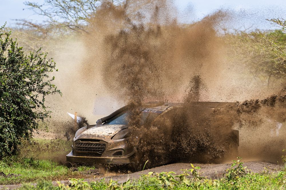 Rally car kicks up dust while racing through a dirt track during an intense off-road competition.