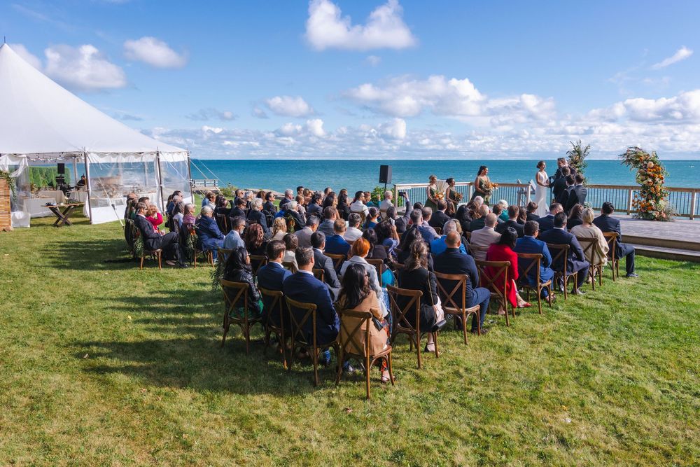 A large group of people seated outdoors on a grassy area with a scenic ocean view in the background.