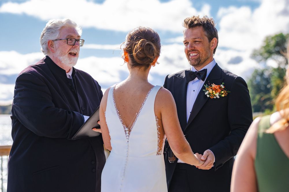 A wedding ceremony with a minister, bride, and groom standing together outdoors.