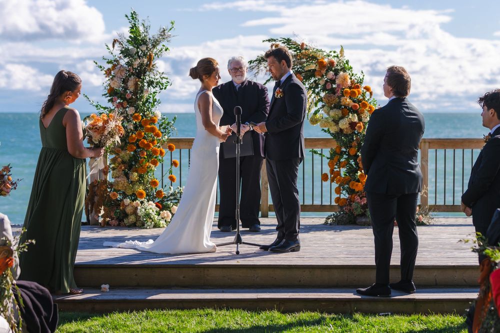 A wedding ceremony taking place outdoors with a scenic ocean view and floral decorations.