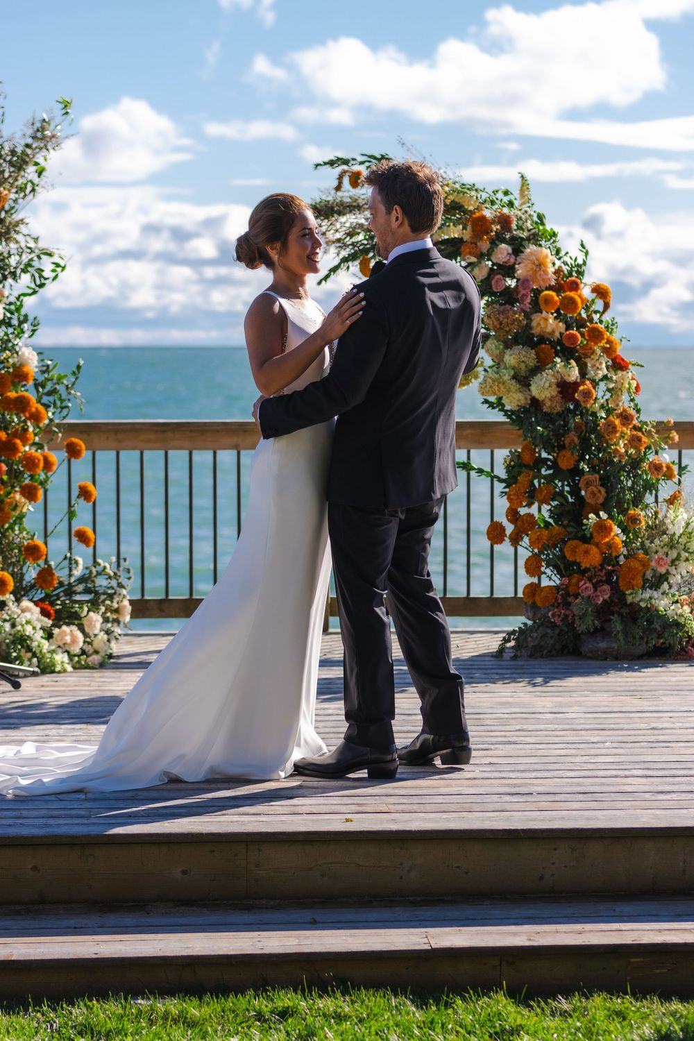 A bride and groom embracing at their wedding ceremony with a floral arch in the background.