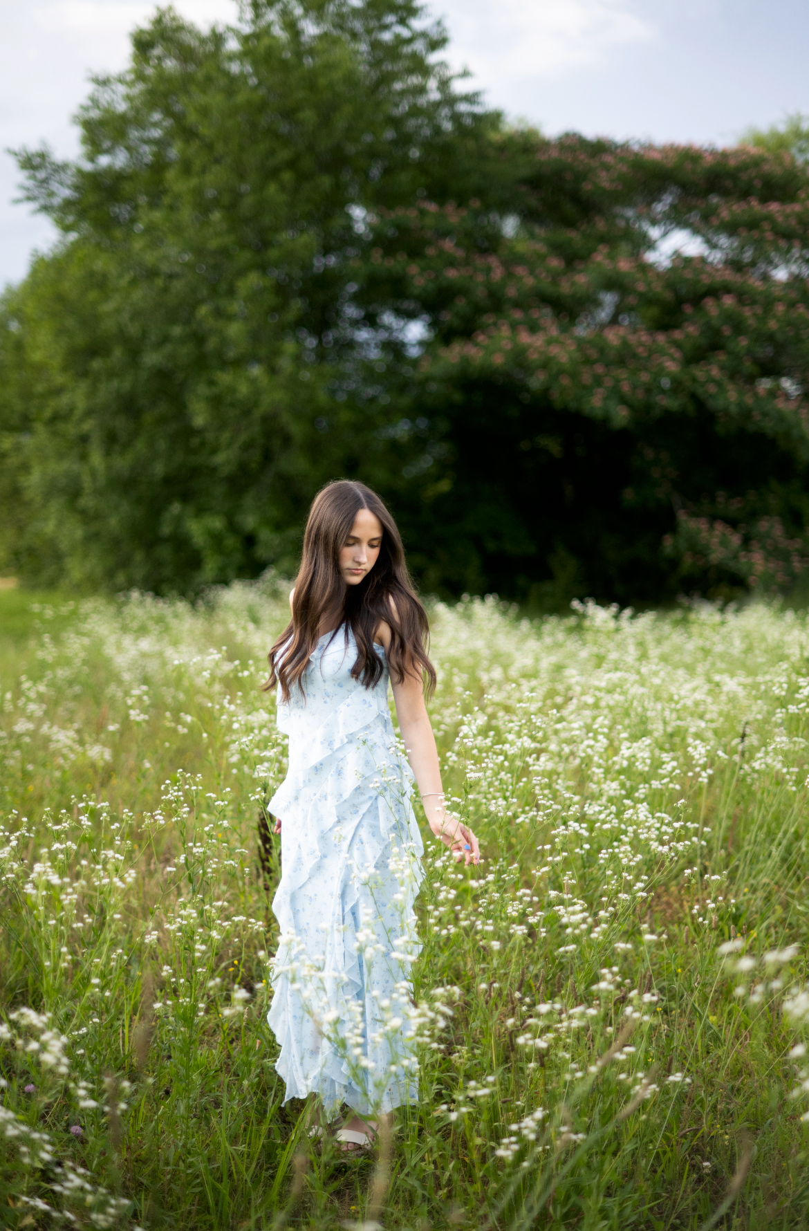 A person in a light blue dress walks through a dreamy summer meadow filled with blooming white daisies and tall grass.