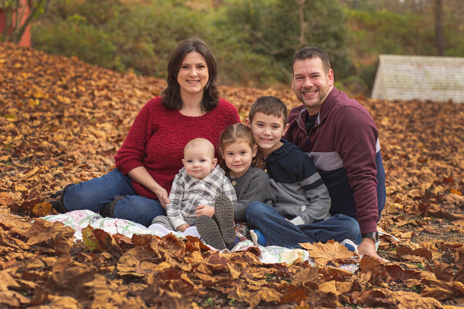 Family of five smiling together outdoors on autumn leaves during fall family portrait photo session.