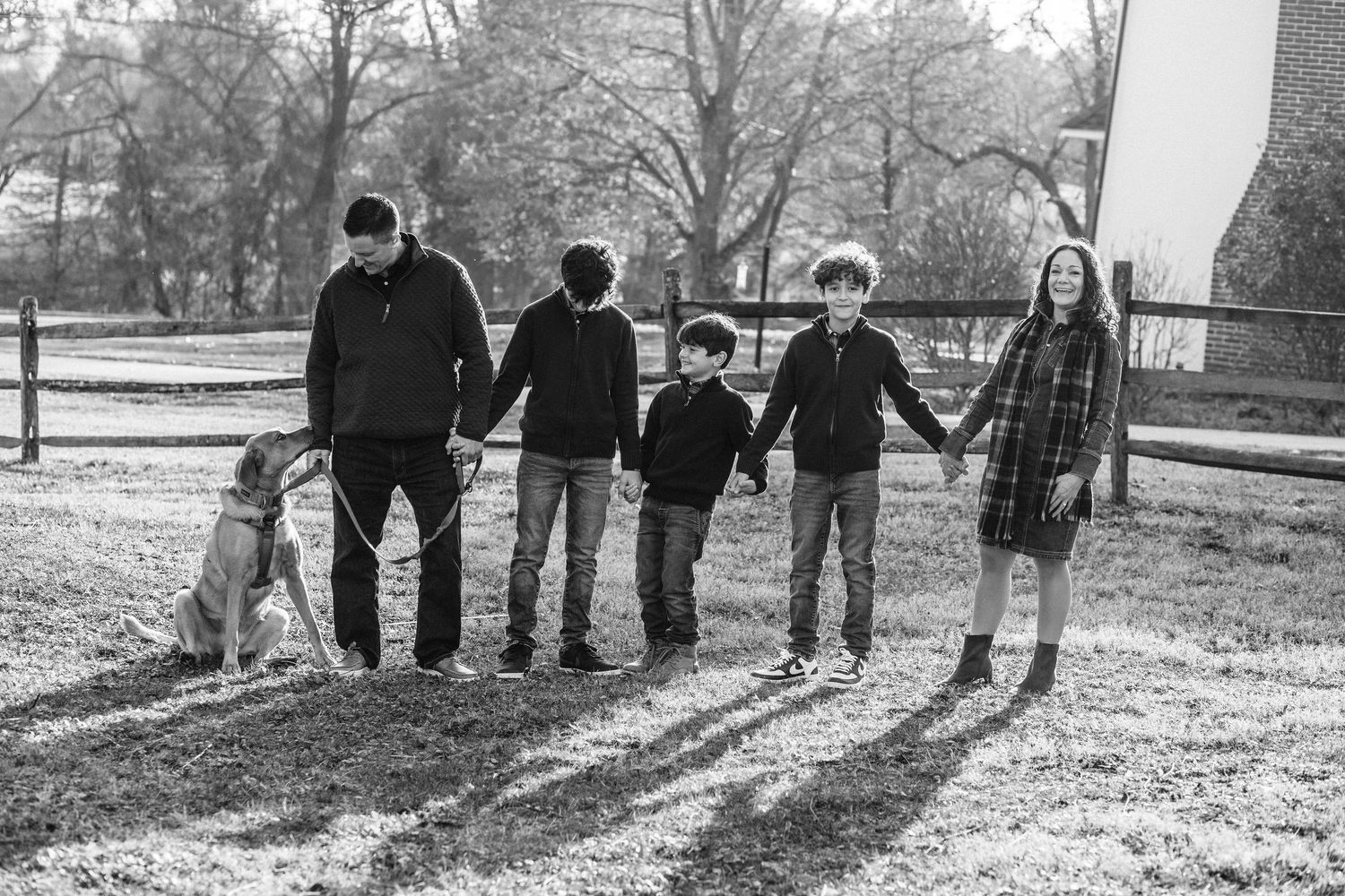 Black and white family photo with parents, four children, and a dog holding hands outdoors in a park.