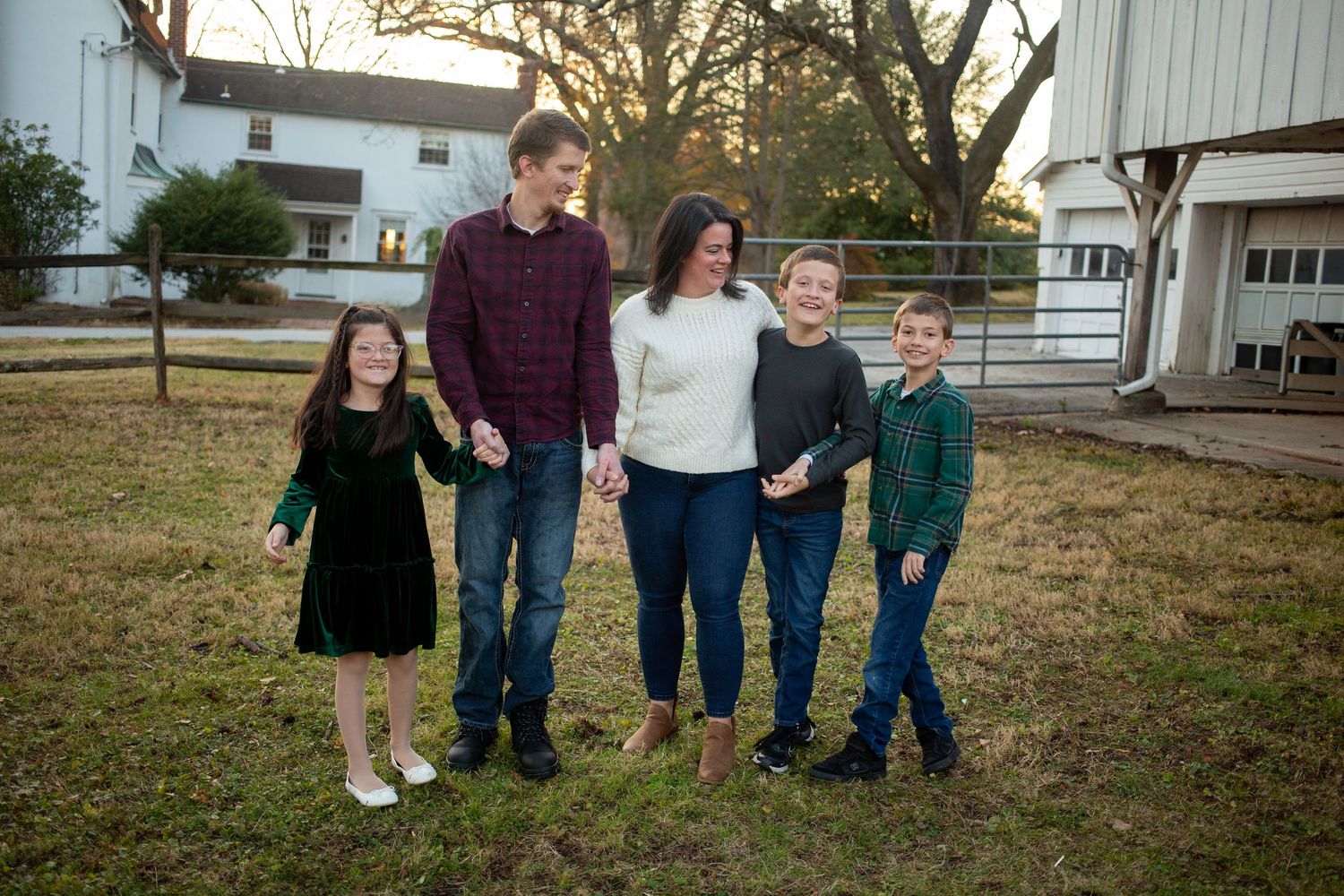 Happy family of five posing outdoors on a farm, parents holding hands with three children in festive green and red attire.