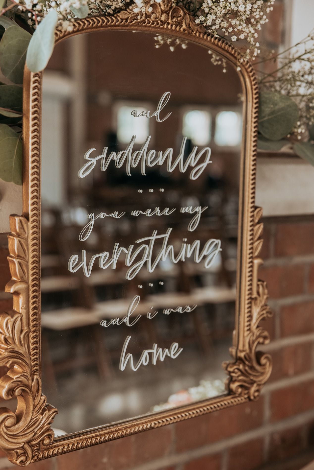 Decorative gold vintage mirror frames with romantic text written in white calligraphy displayed in a wedding venue.