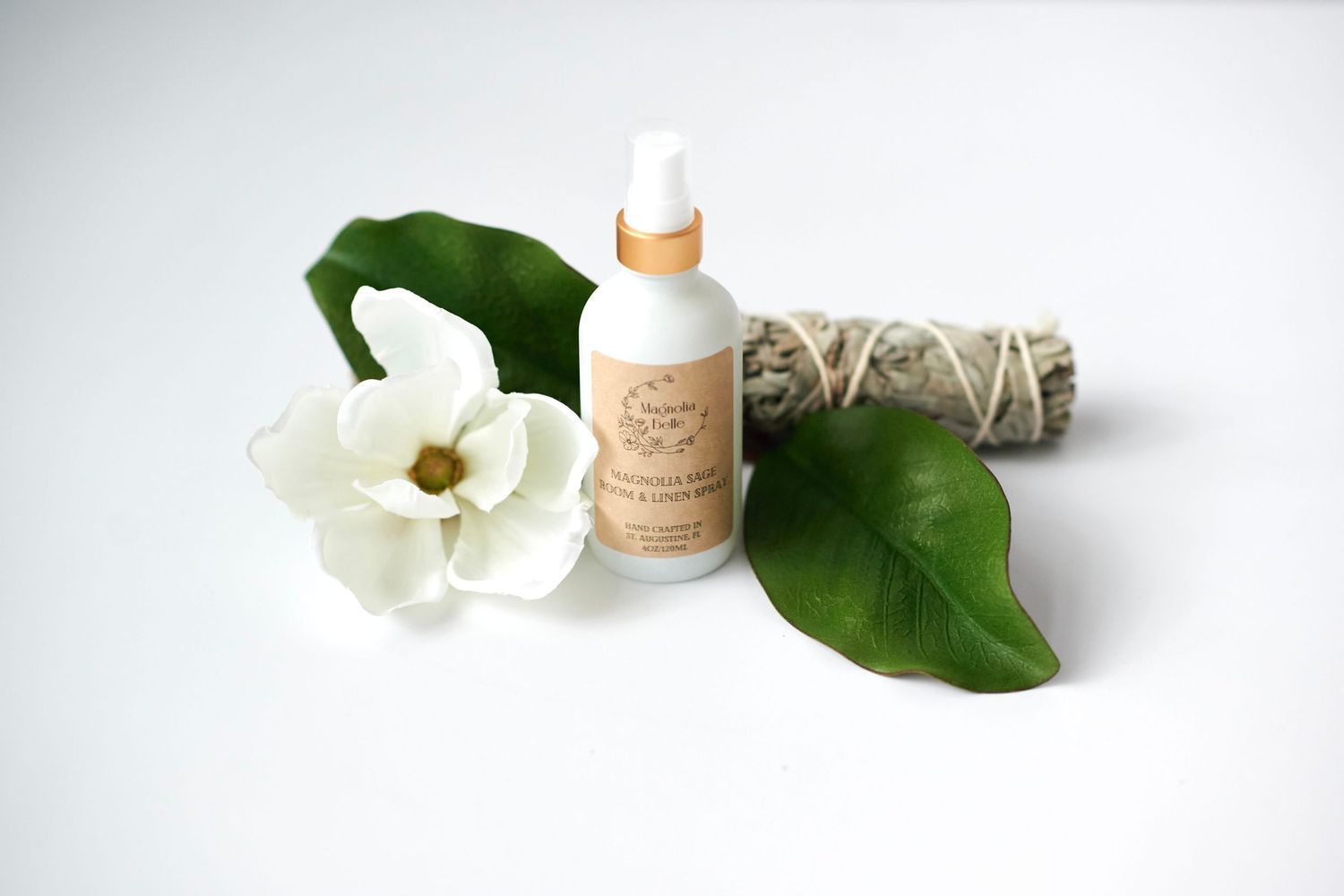 Natural skincare product with white flower, green leaves and sage smudge stick on white background.