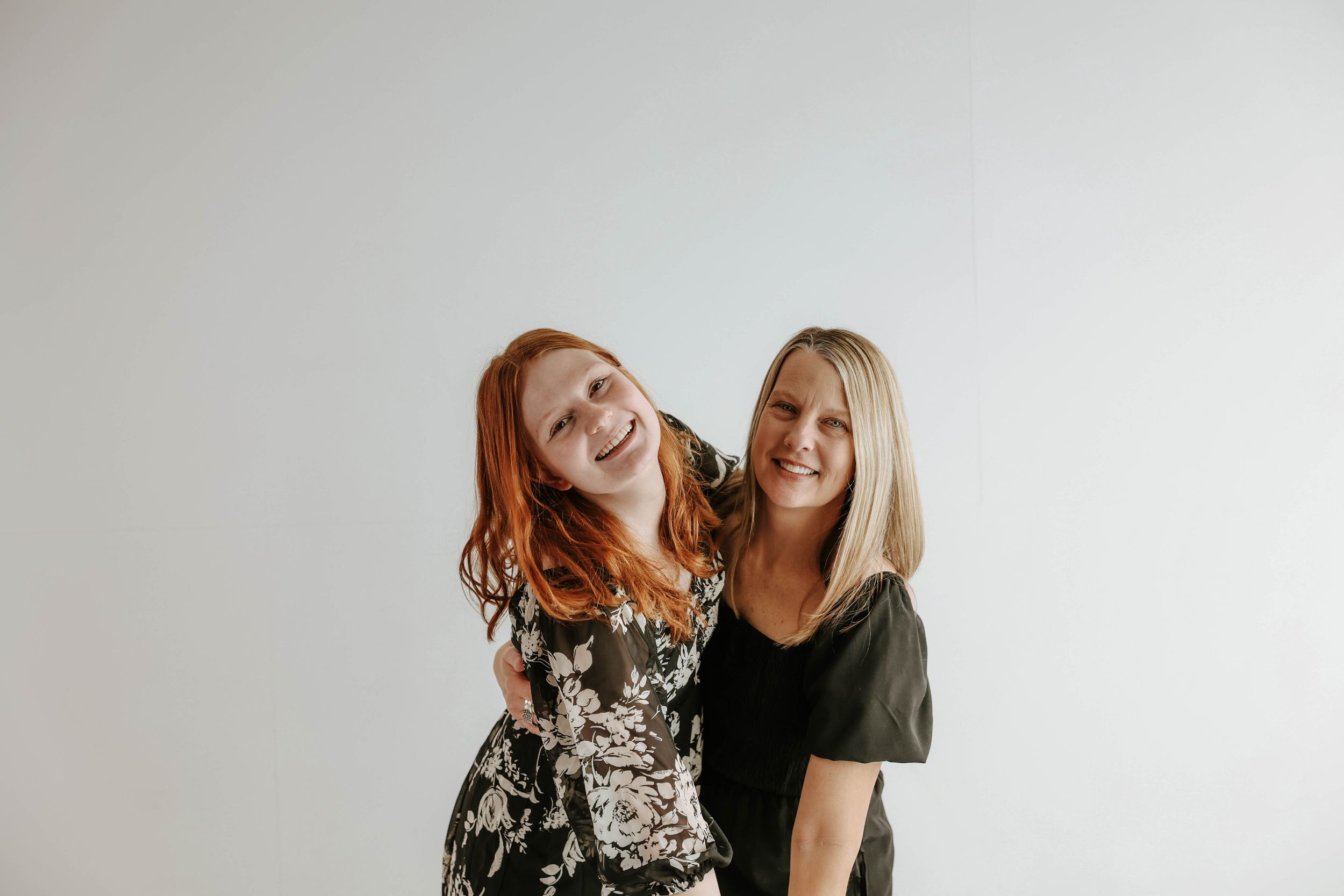 Two people wearing black and white outfits pose and laugh together against a light background.