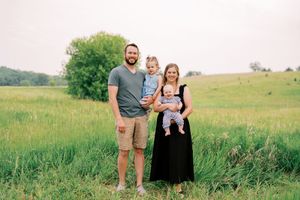 A family enjoying a sunny day in a green meadow with tall grass and trees in the background.
