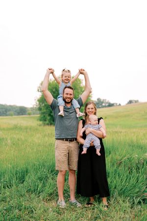 Family enjoying a playful moment together in a lush green meadow during a summer photoshoot.