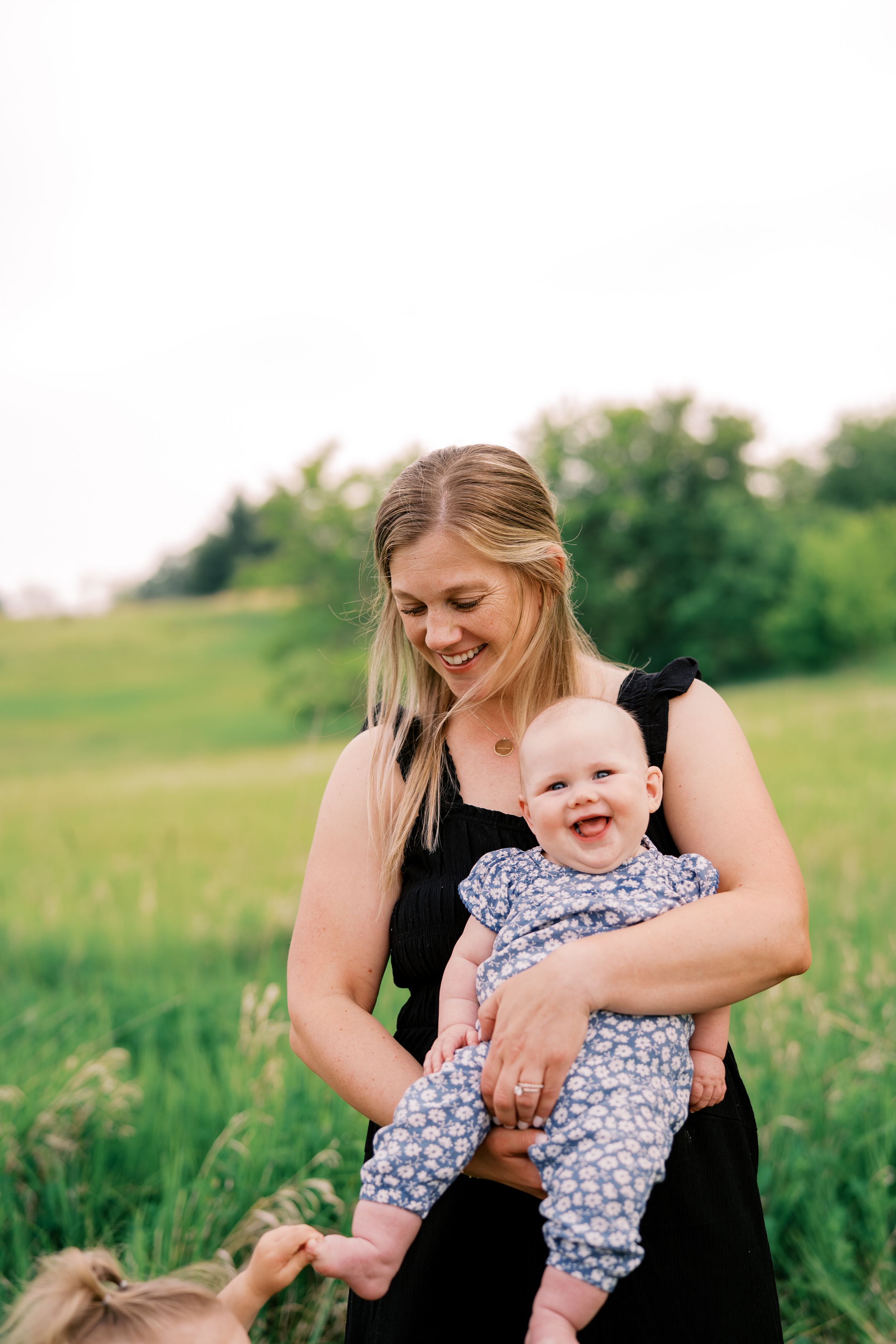 A tender outdoor moment captured in a grassy field with a floral print romper and black dress on a sunny day.