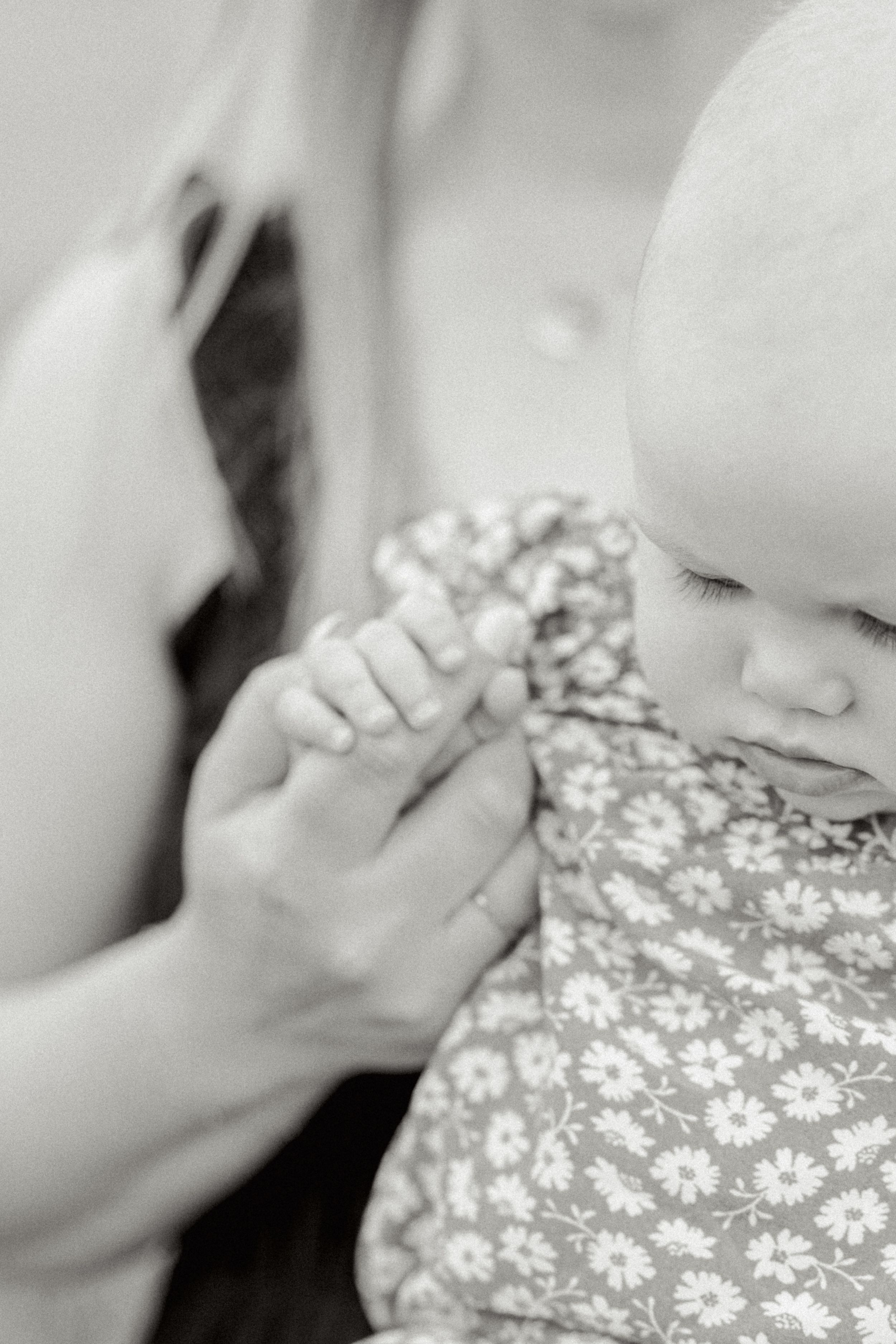 A tender black and white close-up of small hands holding each other against a floral patterned dress.