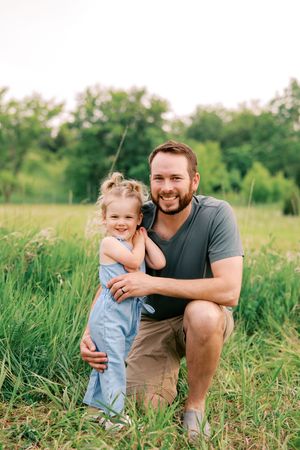 A parent and child share a joyful moment together while posing in a lush green field on a bright summer day.