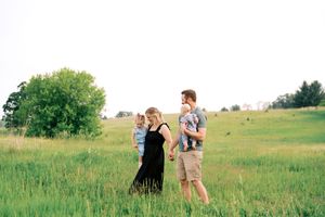 A couple embraces in a sunlit meadow with rolling green hills and trees in the background.