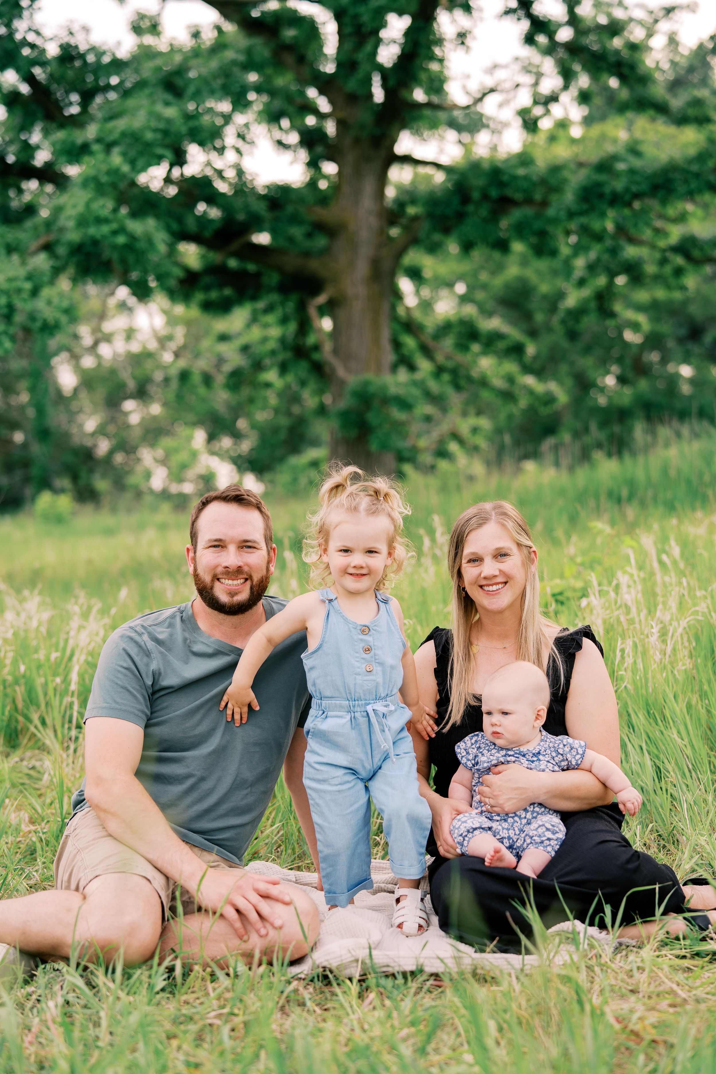 Family sitting together in tall grass during golden hour outdoor photo session.