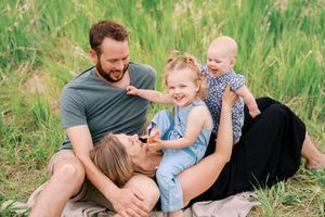 A family enjoys a playful moment together while lying in tall green grass on a sunny day.