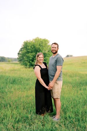 Couple poses together in a scenic meadow during a warm summer evening photoshoot.