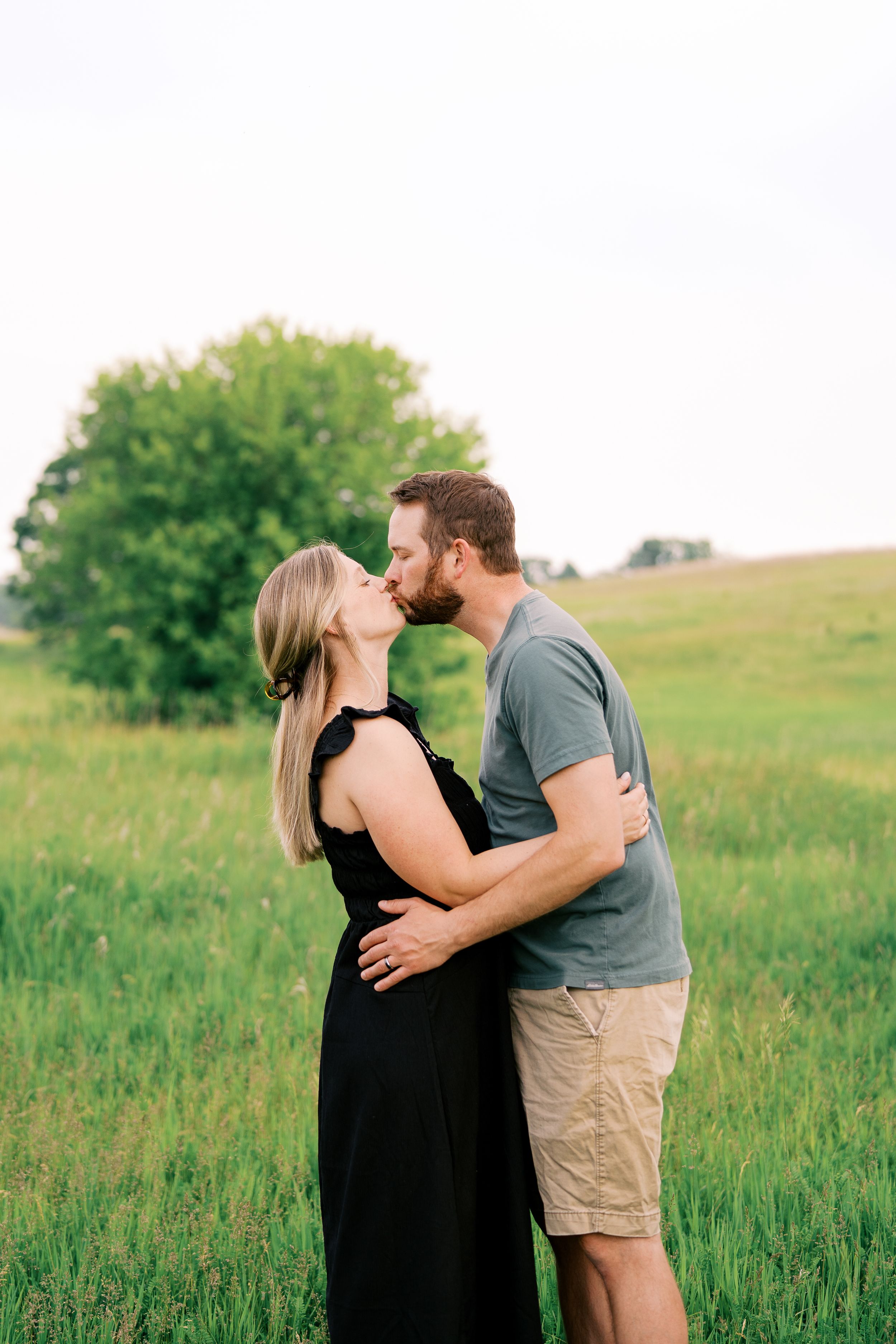 A romantic couple embraces in a green summer meadow during golden hour.