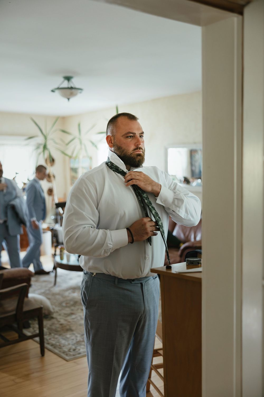 Sequence of four photos showing a man in formal grey attire adjusting his tie while getting ready in a bright room.